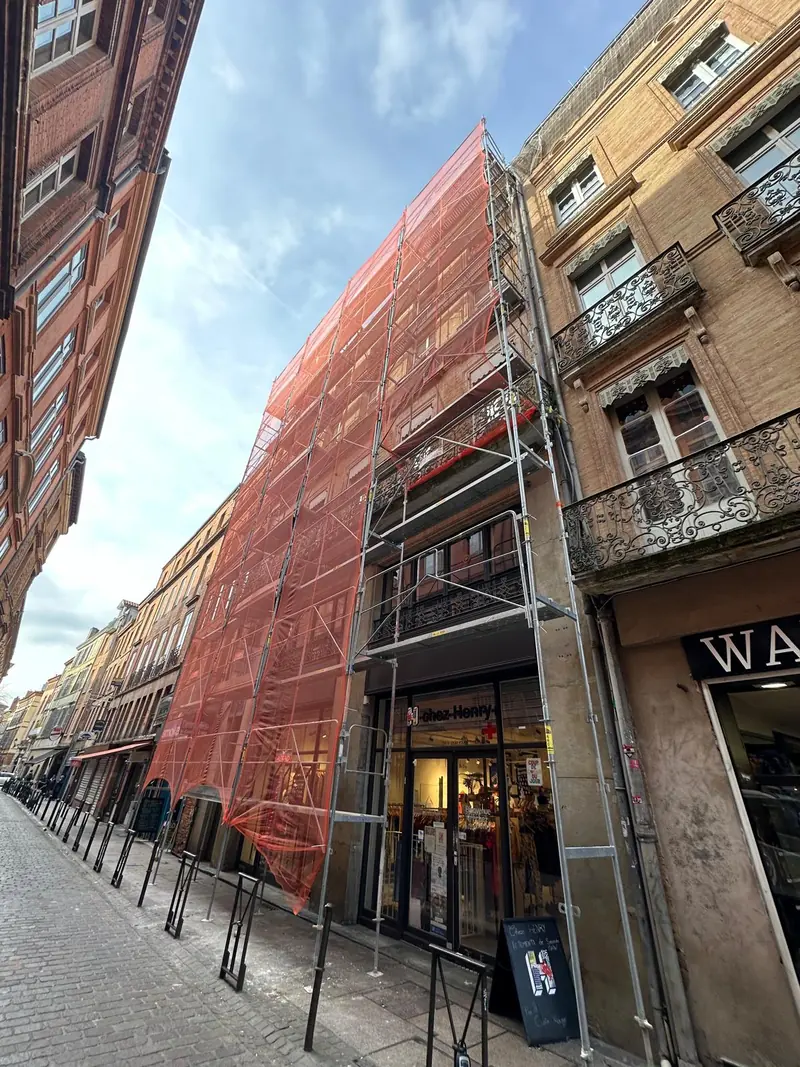 Immeuble en rue commerçante sous échafaudage et filets
